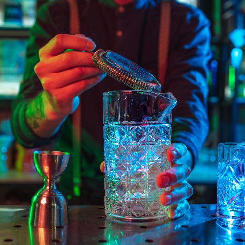 Close up of barman finishes preparation of alcoholic cocktail in multicolored neon light