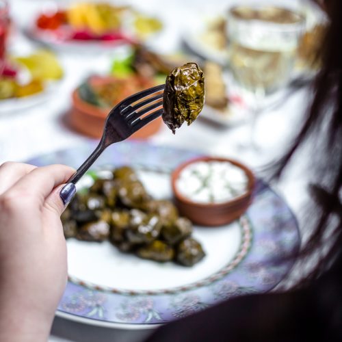 man holds fork with grape leaves dolma plain youghurt side view